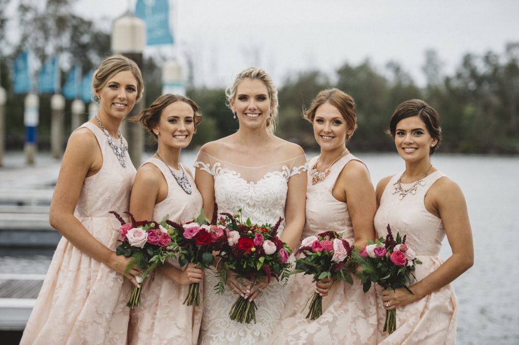 This image showcases a bride and her bridesmaids with their romantic, textured bouquets created by Hart & Flowers, featuring dark pink and blush roses, burgundy amaranthus at a wedding at The Intercontinental Sanctuary Cove.