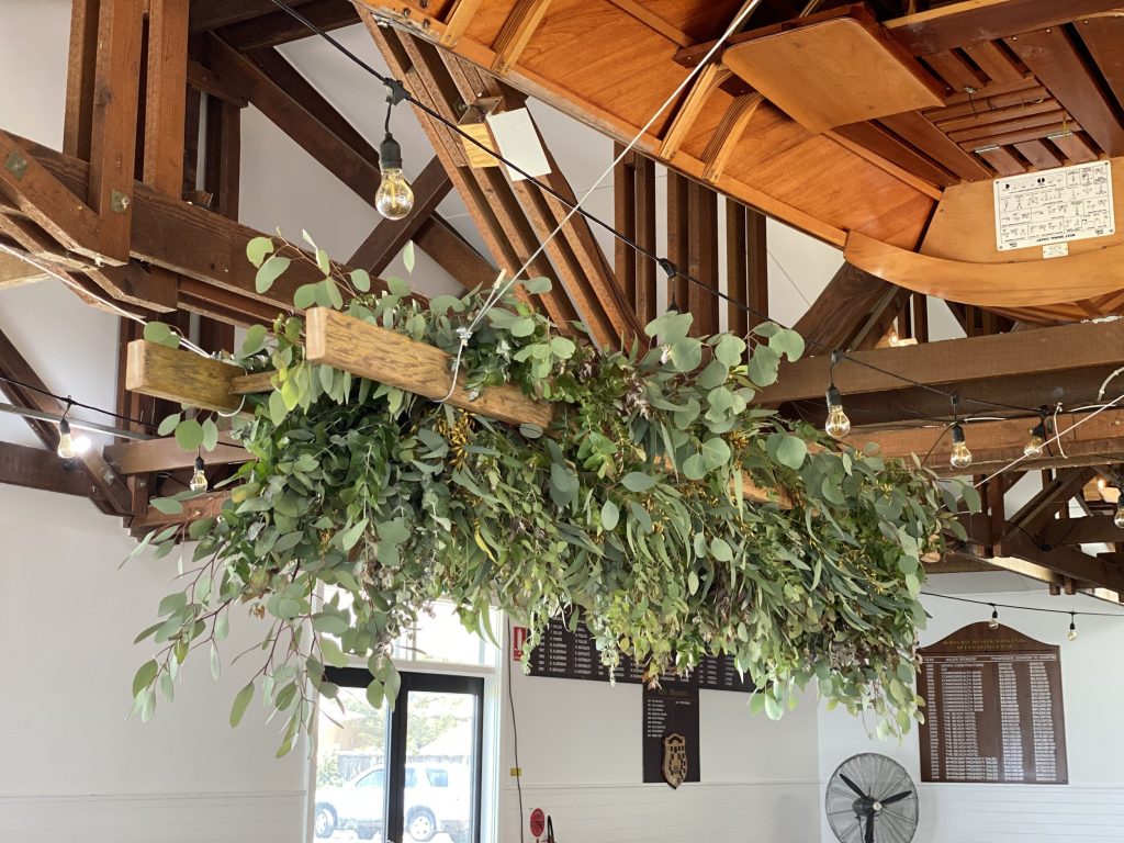 Indoor space with hanging greenery, string lights, wooden ceiling, and large windows