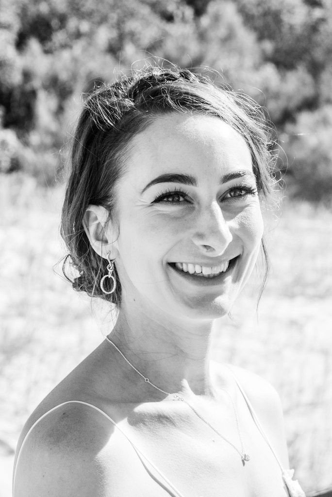 A smiling woman with earrings and a necklace outdoors, black and white photo.