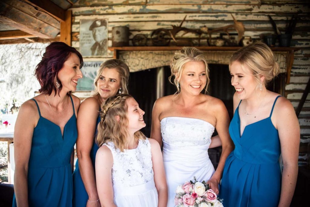 A bride and four women, some possibly bridesmaids, smiling and standing close together in a rustic setting with wood walls and vintage decor.