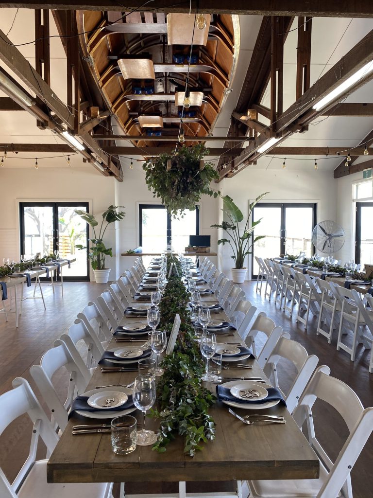 A rustic and romantic wedding installation featuring a wooden ladder adorned with lush greenery. The ladder is draped with fragrant eucalyptus leaves, creating a textural and inviting backdrop for the ceremony or reception. The natural elements of th