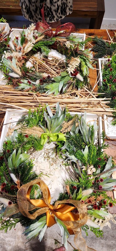 Beautiful Christmas wreaths made of various greenery, flowers, and decorative ribbons displayed on a table.