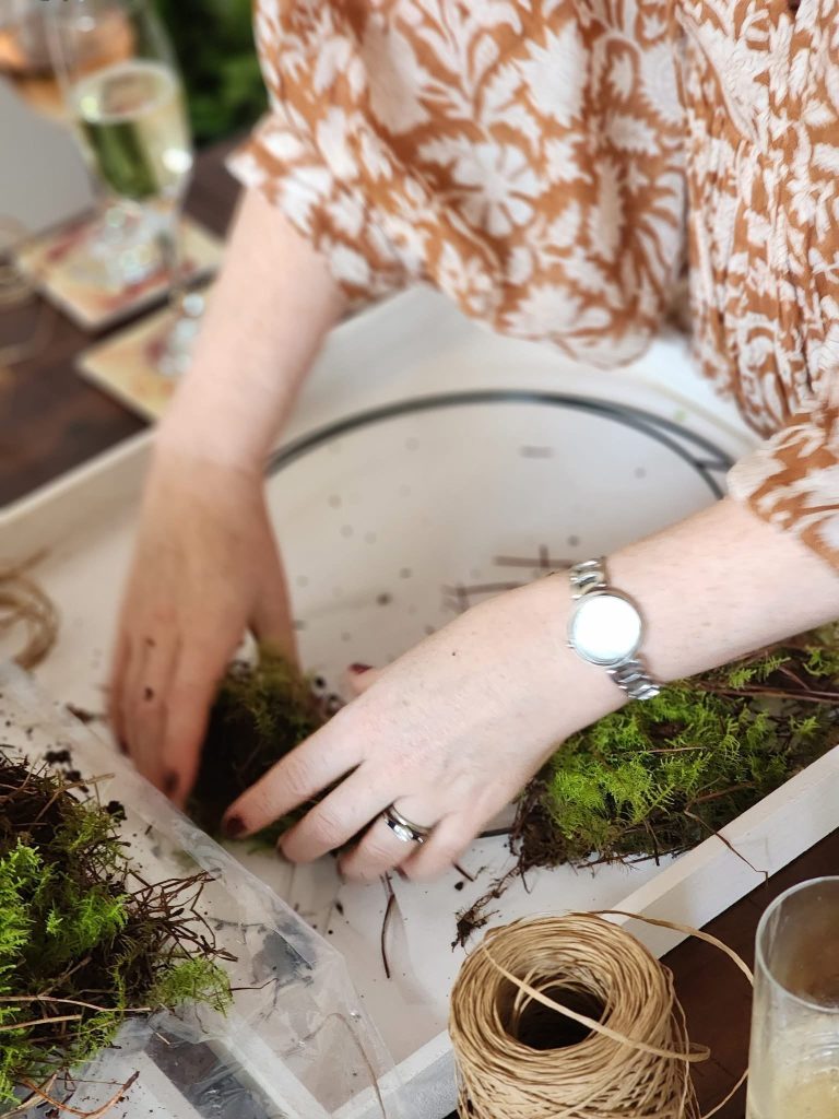 Person arranging moss and natural materials in a tray for crafting.