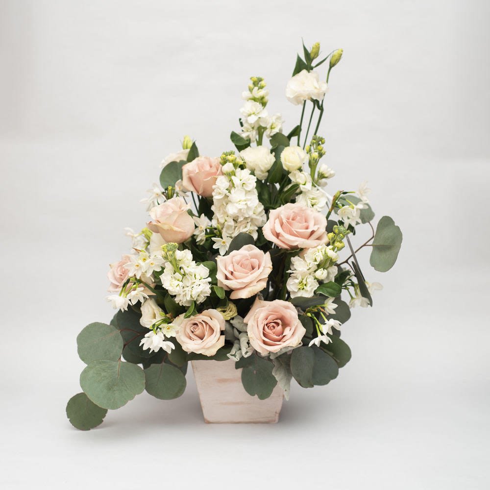 A timeless and elegant floral arrangement featuring a soft palette of blush and white. The arrangement showcases a mix of roses, lisianthus, and greenery, creating a textural and captivating display. The overall effect is one of understated elegance