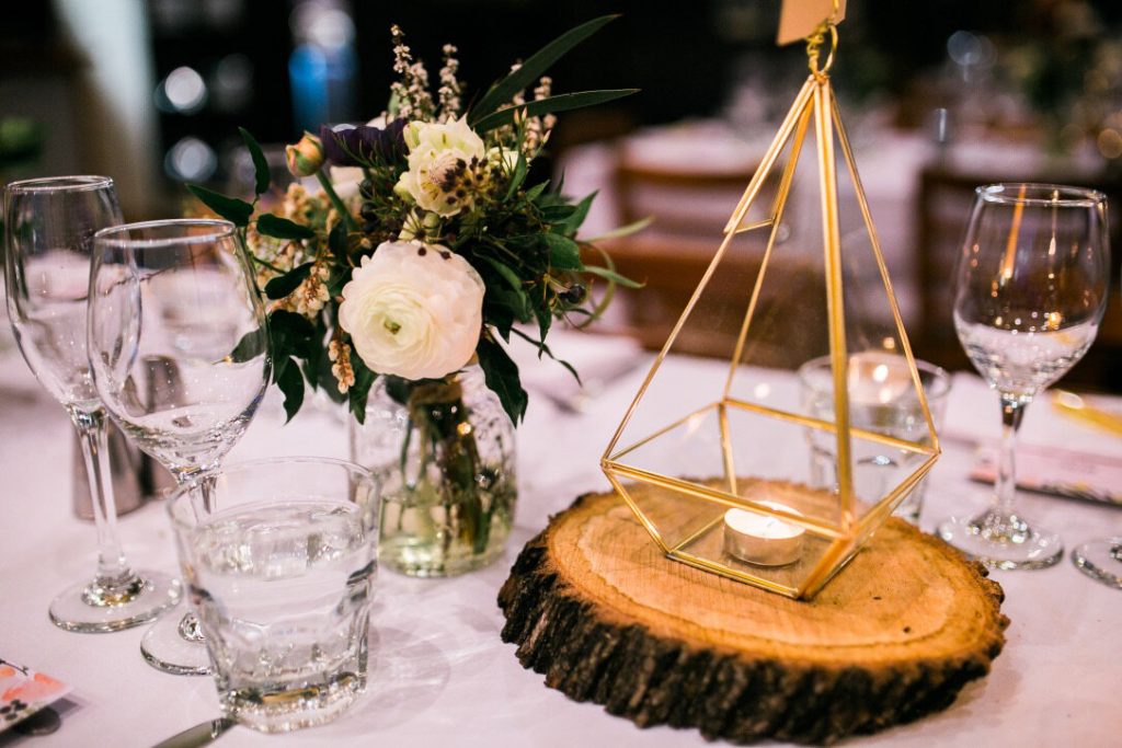 Elegant table centerpiece with a floral arrangement, gold geometric decor with a candle, and glassware on a table.